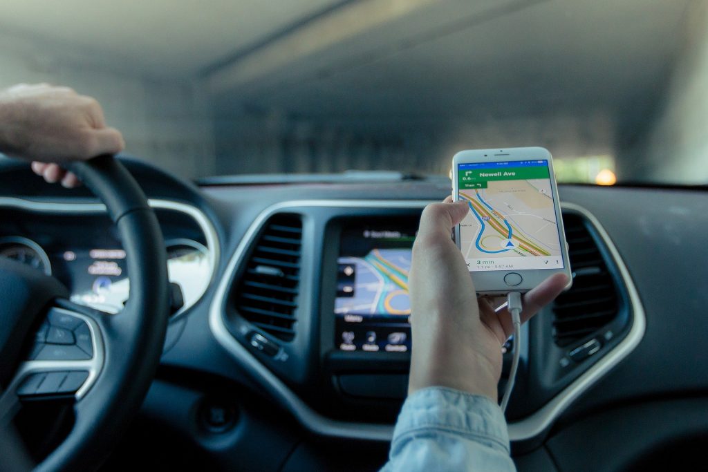 Uma pessoa dirigindo um carro, com outra pessoa segurando um telefone. Imagem ilustrativa para o texto seguro para táxis e ubers.
