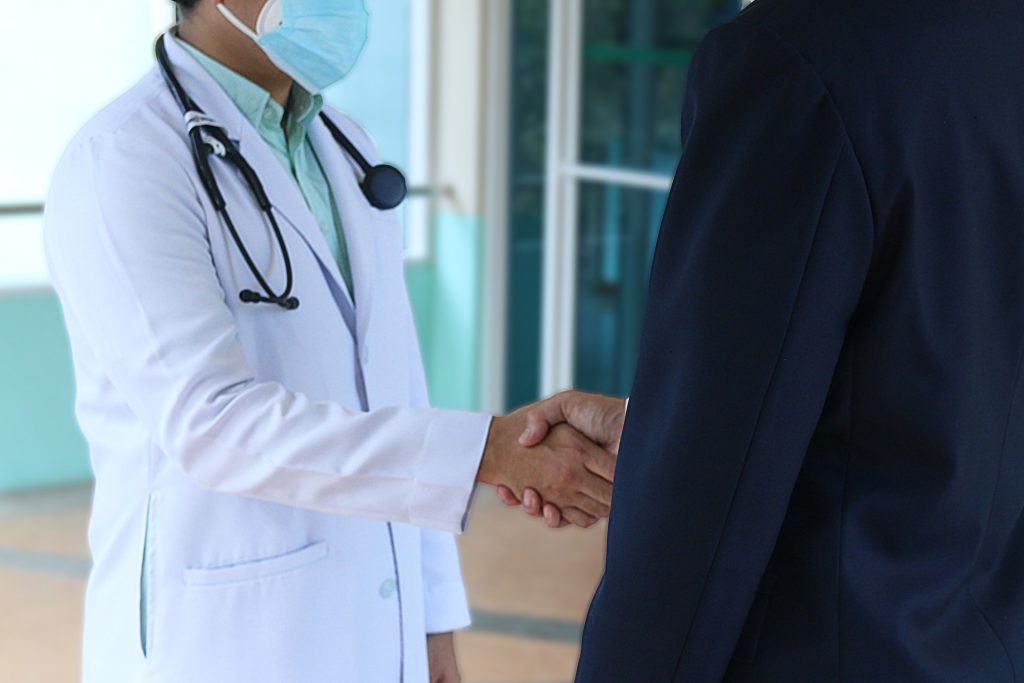 Foto de uma pessoa de terno, apertando a mão de um médico com jaleco e estetoscópio. Imagem ilustrativa para o texto seguro saúde e plano de saúde.