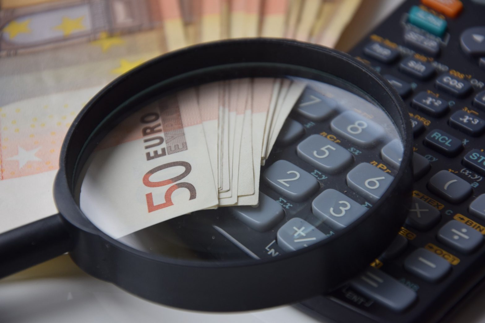 Foto de uma lupa com notas de dinheiro e uma calculadora. Imagem ilustrativa para o texto valor da franquia do seguro.